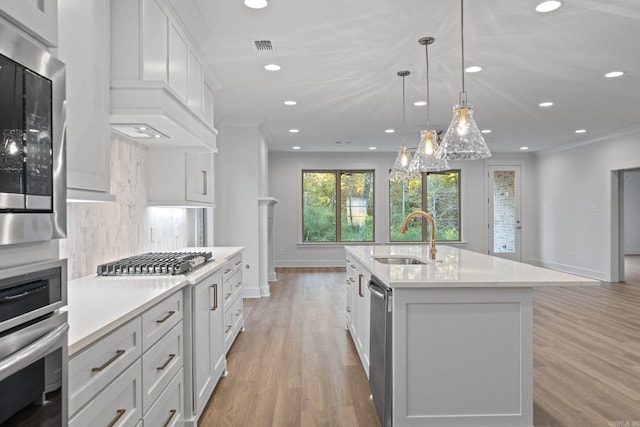 kitchen featuring sink, an island with sink, pendant lighting, white cabinets, and appliances with stainless steel finishes