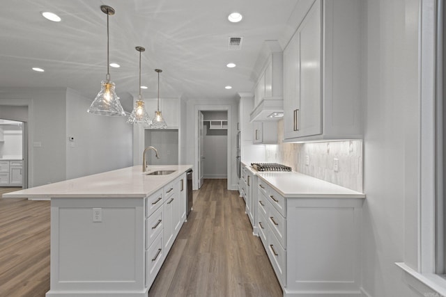 kitchen with a center island with sink, white cabinetry, hanging light fixtures, and sink