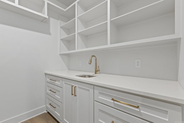 bar featuring hardwood / wood-style flooring, white cabinetry, and sink