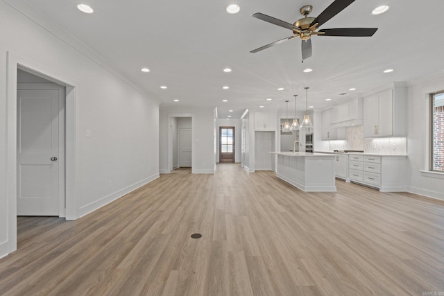 unfurnished living room featuring light wood-type flooring, ceiling fan, ornamental molding, and sink