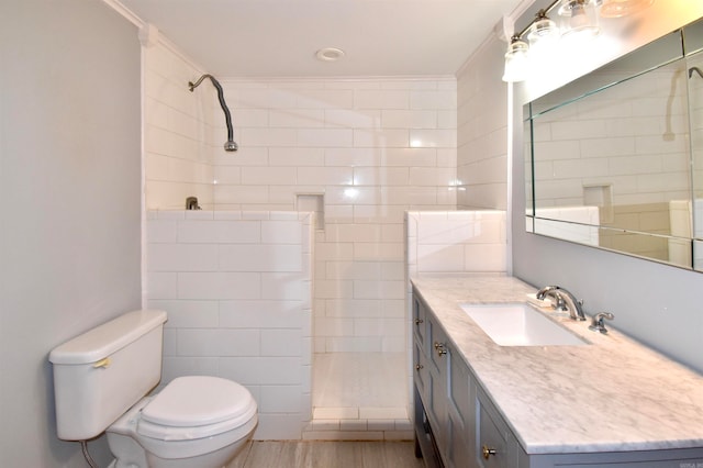 bathroom featuring ornamental molding, a tile shower, vanity, hardwood / wood-style flooring, and toilet