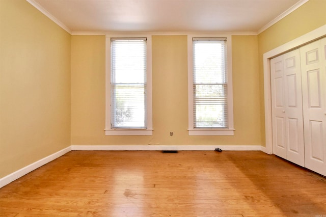 unfurnished bedroom featuring a closet, multiple windows, crown molding, and light hardwood / wood-style flooring