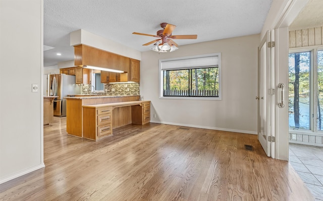 kitchen featuring stainless steel fridge with ice dispenser, kitchen peninsula, a textured ceiling, and light hardwood / wood-style flooring