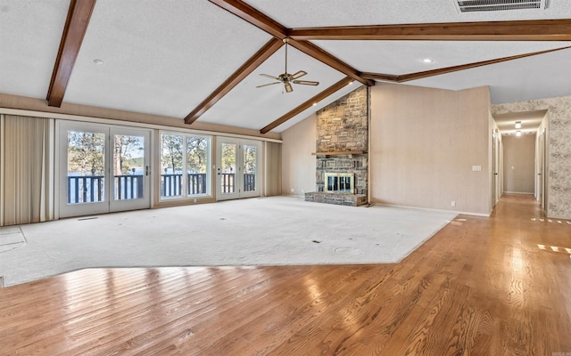 unfurnished living room featuring vaulted ceiling with beams, a stone fireplace, a textured ceiling, and light hardwood / wood-style flooring