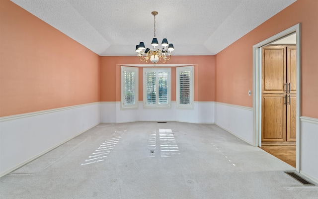 carpeted spare room featuring a textured ceiling, vaulted ceiling, and a notable chandelier