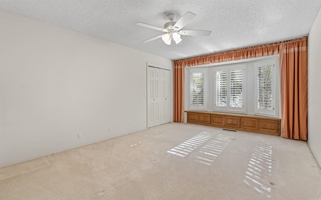 unfurnished bedroom featuring light carpet, a textured ceiling, a closet, and ceiling fan