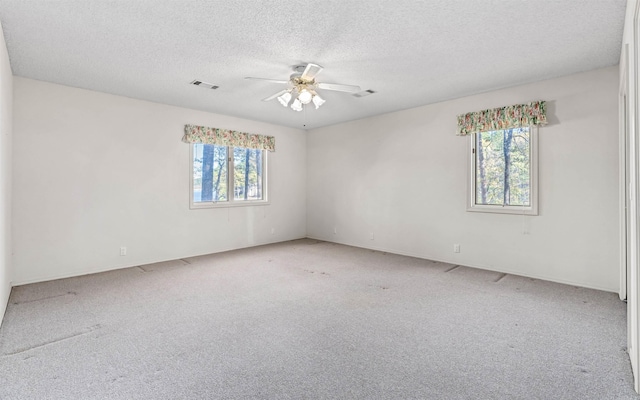 carpeted spare room with a textured ceiling, ceiling fan, and a healthy amount of sunlight