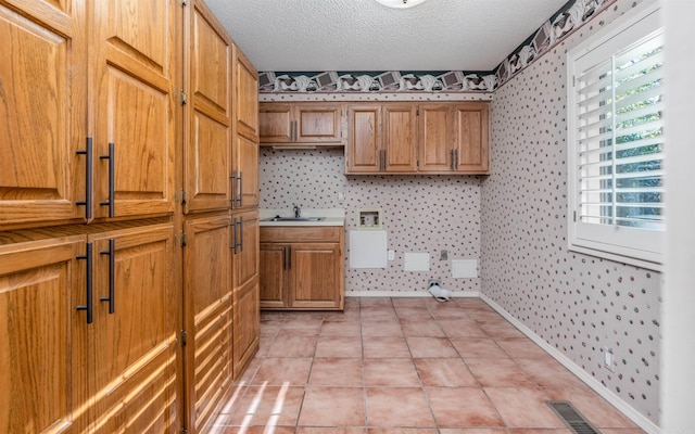 laundry area featuring sink, light tile patterned floors, cabinets, and a textured ceiling