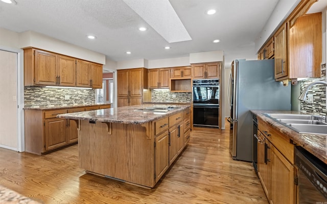 kitchen with sink, a center island, light hardwood / wood-style flooring, backsplash, and black appliances