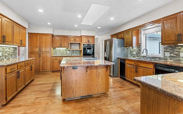 kitchen featuring a skylight, light stone countertops, a center island, light hardwood / wood-style floors, and black appliances