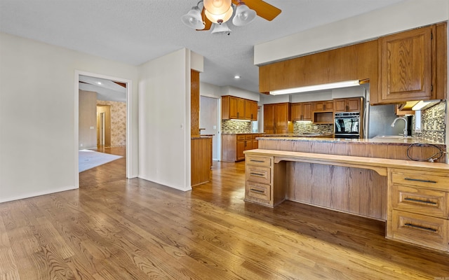 kitchen with a textured ceiling, oven, light wood-type flooring, and sink