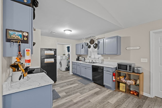 kitchen with light wood-type flooring, gray cabinetry, sink, black appliances, and washing machine and clothes dryer