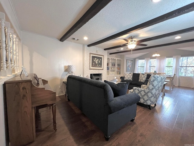 living room featuring beam ceiling, ceiling fan, a brick fireplace, dark hardwood / wood-style flooring, and a textured ceiling