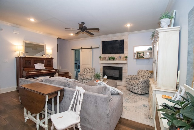 living room with ceiling fan, crown molding, a barn door, a fireplace, and dark hardwood / wood-style floors