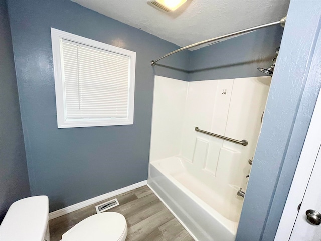 bathroom featuring bathtub / shower combination, wood-type flooring, toilet, and a textured ceiling