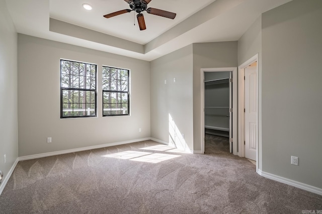 unfurnished bedroom with a tray ceiling, ceiling fan, a spacious closet, carpet floors, and a closet