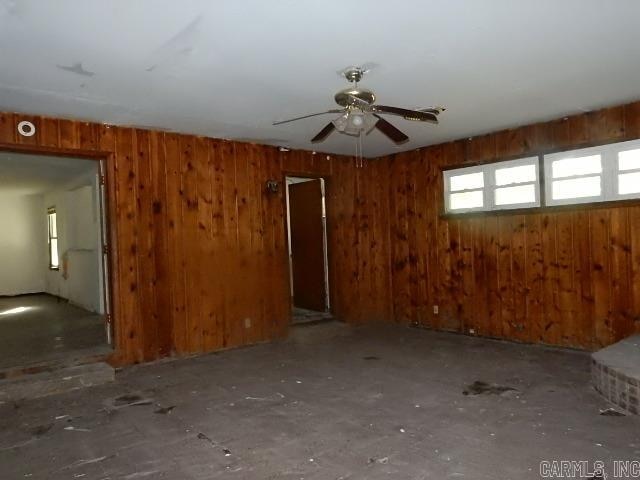 empty room featuring ceiling fan and wooden walls