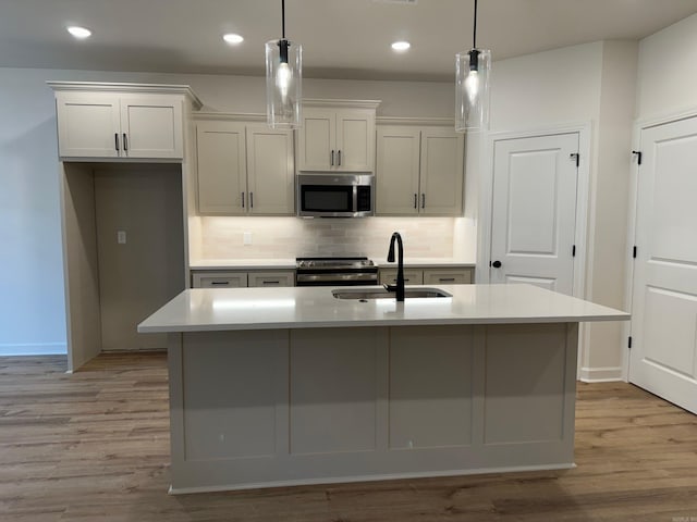 kitchen with decorative light fixtures, an island with sink, stainless steel appliances, and sink