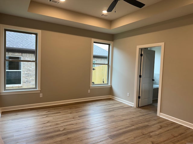 empty room with ceiling fan, light hardwood / wood-style floors, and a raised ceiling