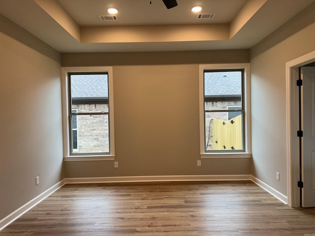 empty room with light hardwood / wood-style floors, ceiling fan, and a tray ceiling