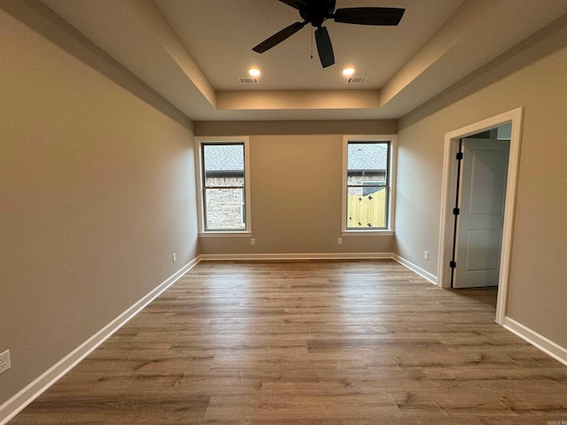 empty room with a tray ceiling, ceiling fan, and light wood-type flooring