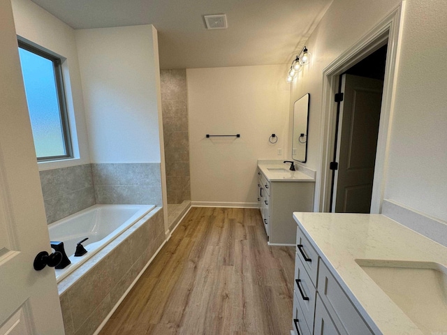 bathroom with hardwood / wood-style flooring, vanity, and tiled bath