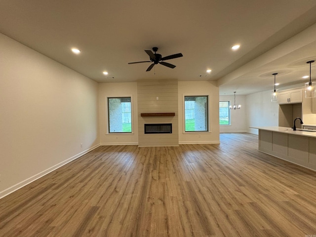 unfurnished living room featuring a large fireplace, light hardwood / wood-style flooring, ceiling fan with notable chandelier, and sink