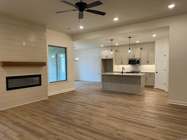 kitchen featuring light wood-type flooring, a center island with sink, white cabinetry, and hanging light fixtures