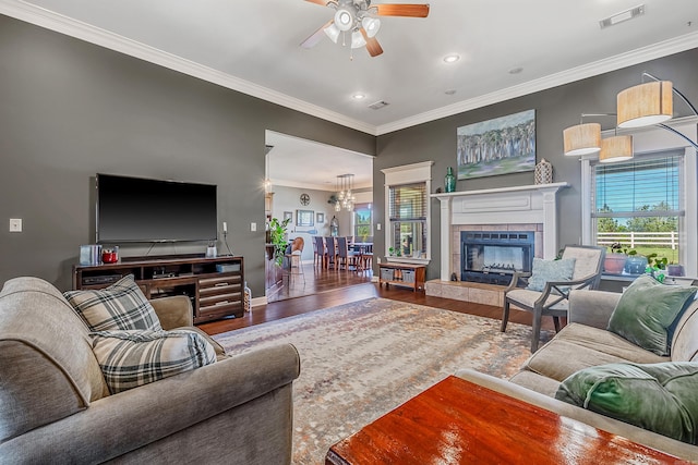 living room with a tiled fireplace, crown molding, ceiling fan, and wood-type flooring