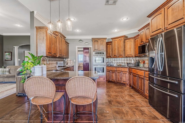 kitchen with ornate columns, crown molding, a breakfast bar, and stainless steel appliances