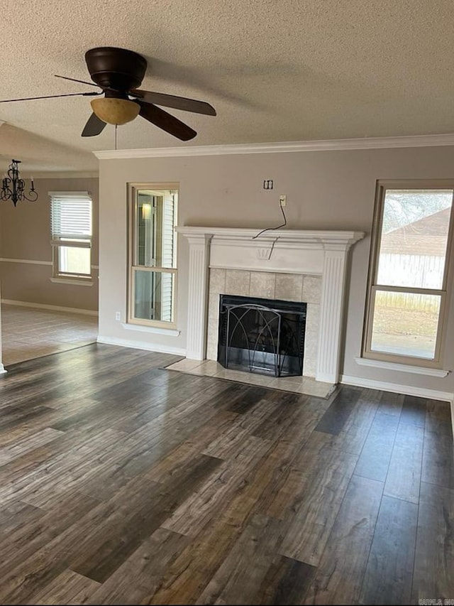 unfurnished living room featuring dark wood-type flooring, crown molding, a textured ceiling, a fireplace, and ceiling fan with notable chandelier