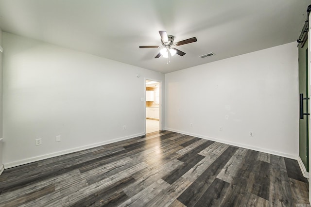 empty room with a barn door, dark hardwood / wood-style floors, and ceiling fan