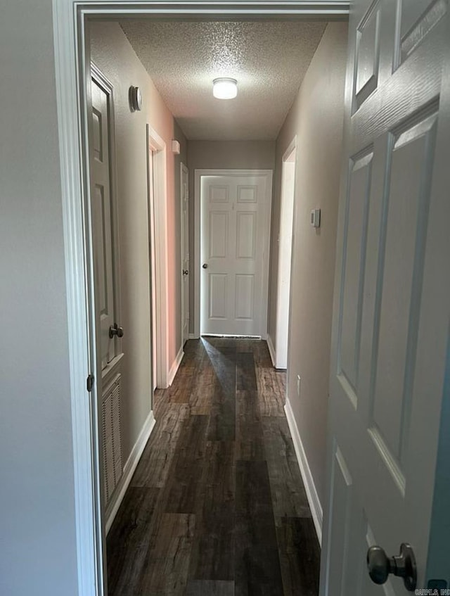 corridor with dark hardwood / wood-style flooring and a textured ceiling