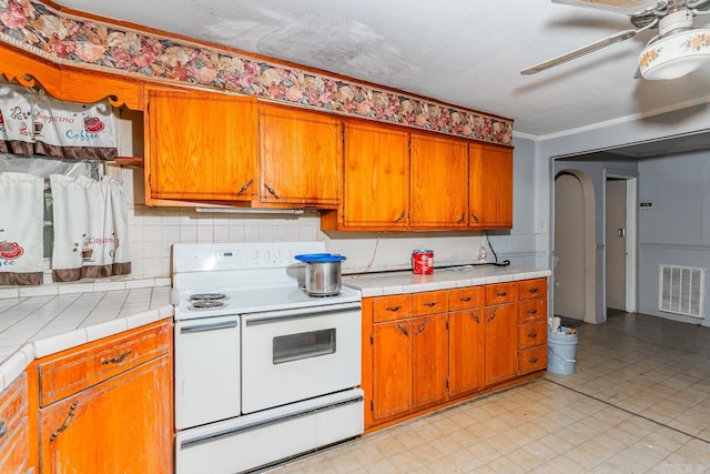 kitchen featuring backsplash, ceiling fan, crown molding, tile countertops, and white range with electric cooktop