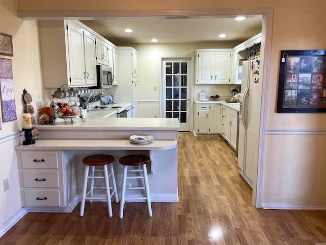 kitchen with white appliances, a breakfast bar area, kitchen peninsula, and white cabinets