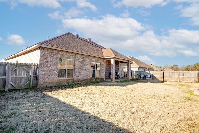 back of property with a yard, brick siding, a shingled roof, and a fenced backyard