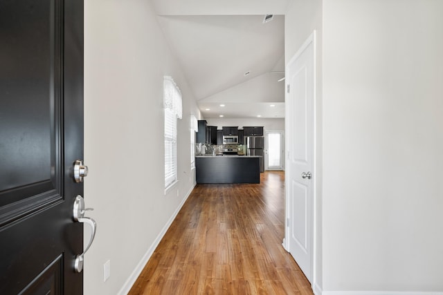 corridor with wood-type flooring and vaulted ceiling