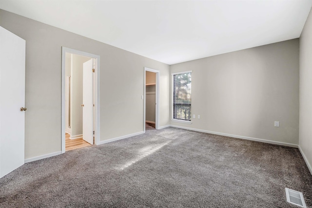 unfurnished bedroom with carpet, a closet, a walk in closet, and ensuite bath