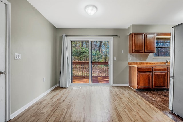 interior space with stainless steel fridge, light wood-type flooring, and backsplash