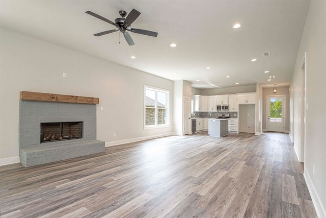 unfurnished living room with ceiling fan, a fireplace, a healthy amount of sunlight, and light wood-type flooring