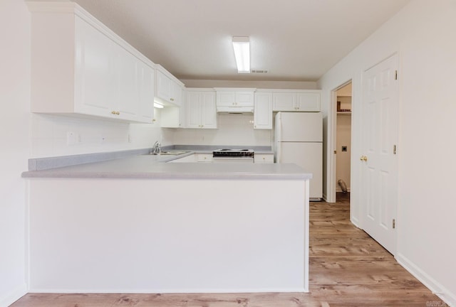 kitchen with sink, light hardwood / wood-style flooring, white cabinets, stainless steel gas stove, and white fridge