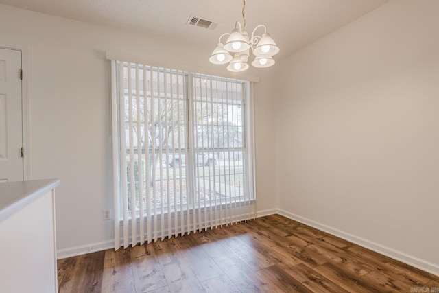 unfurnished dining area featuring dark wood-type flooring and a notable chandelier