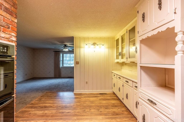 713 N Spring St, Searcy, AR 72143 - kitchen featuring a textured ceiling, a ceiling fan, light countertops, glass insert cabinets, and light wood-type flooring