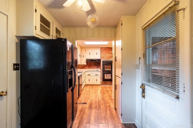 713 N Spring St, Searcy, AR 72143 - kitchen with black appliances, under cabinet range hood, light wood-style flooring, a textured ceiling, and white cabinets