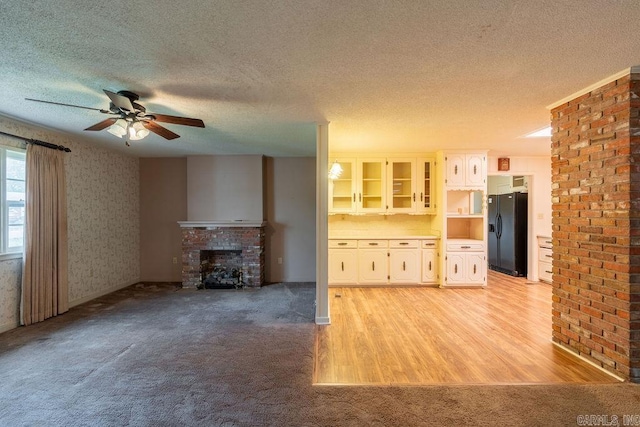 713 N Spring St, Searcy, AR 72143 - unfurnished living room featuring a textured ceiling, ceiling fan, a brick fireplace, light colored carpet, and light wood-style floors
