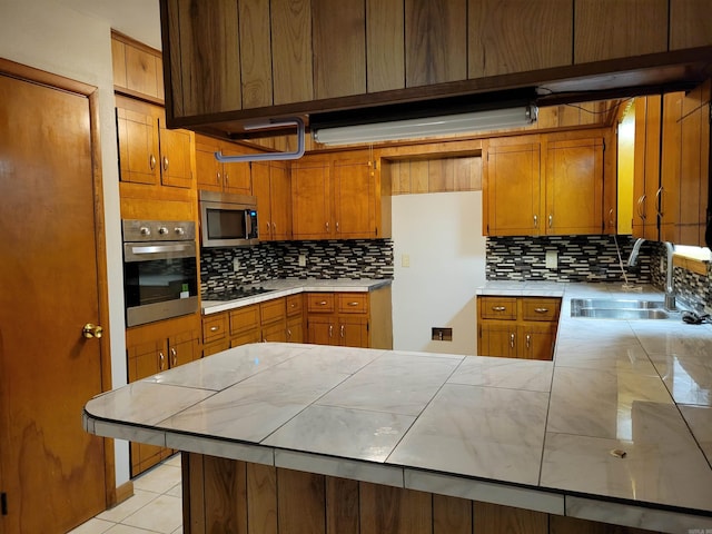 kitchen with kitchen peninsula, appliances with stainless steel finishes, backsplash, sink, and tile countertops