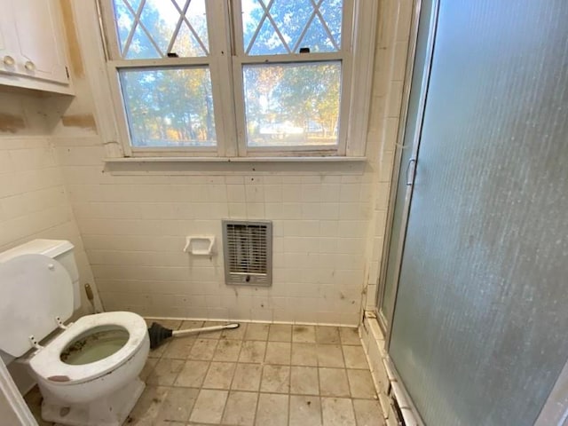 bathroom with heating unit, toilet, and a shower with door