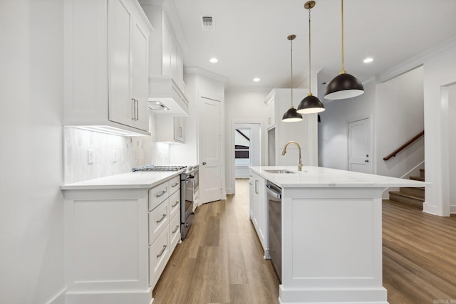 kitchen with white cabinetry, sink, hanging light fixtures, stainless steel appliances, and an island with sink