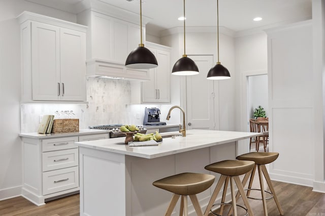 kitchen featuring white cabinetry, a kitchen island with sink, hardwood / wood-style floors, and hanging light fixtures