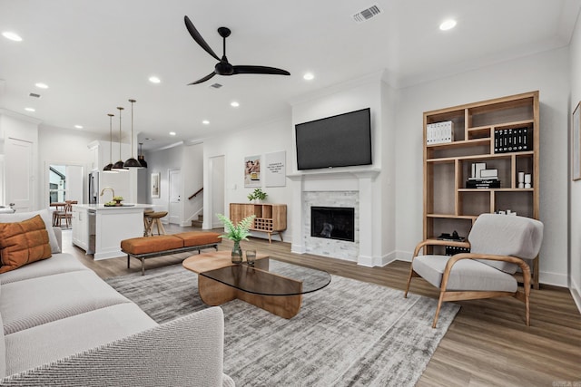 living room with ceiling fan, sink, light wood-type flooring, and ornamental molding